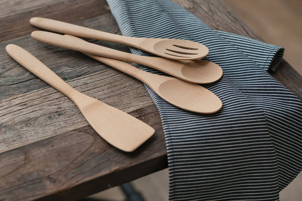 A set of 4 organic bamboo cooking utensils are laid on a stiped dishcloth.