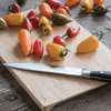 A Large Undercut Series Cutting Board holds a pile of small colorful peppers. A chefs knife is resting on the board - bambu