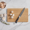 a Large Undercut Series Cutting Board is on a marble countertop. There are mushrooms and garlic nearby, ready to be chopped.- bambu