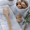 A Scraping Spatula lays on a flour sack kitchen towel next to a bowl of eggs.