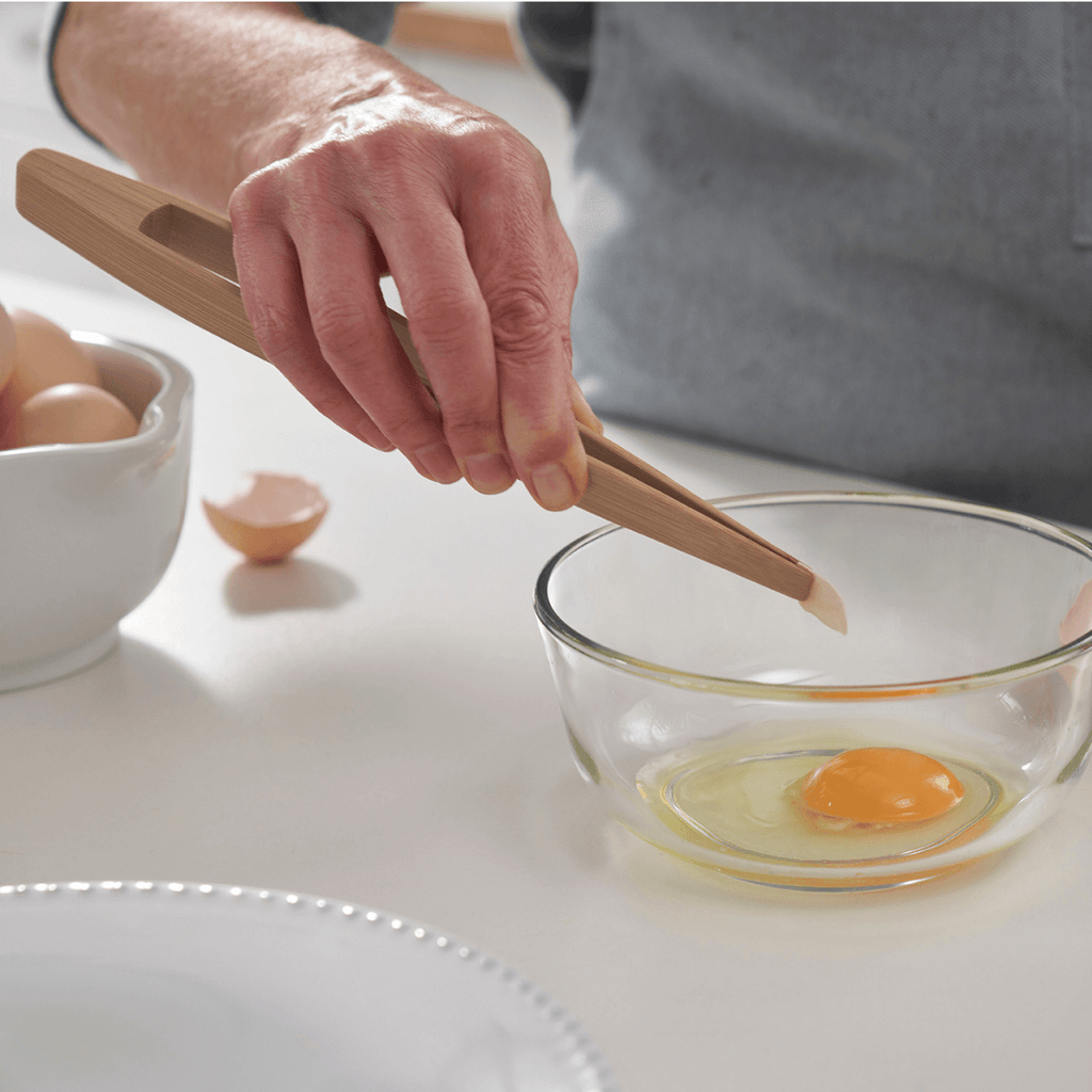 A person uses Large Bamboo Tongs to remove a piece of eggshell from a bowl.