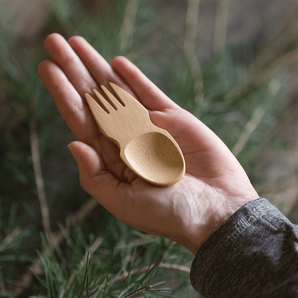 A bamboo spork in held in the palm of an outstretched  hand