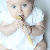 A young baby holds an Organic Bamboo Baby's Feeding Spoon (6M+)