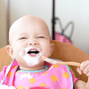 A young baby in a pink and orange polka-dot bib eats yogurt with an Organic Bamboo Baby's Feeding Spoon (6M+) 