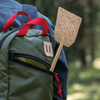 A Bamboo & Cork Fly Swatter is carried in an outer pocket of a green backpack.