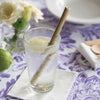 A drinking glass with water and lemon also holds a Reusable Bamboo Straw. The glass is on a table with a purple floral tablecloth.