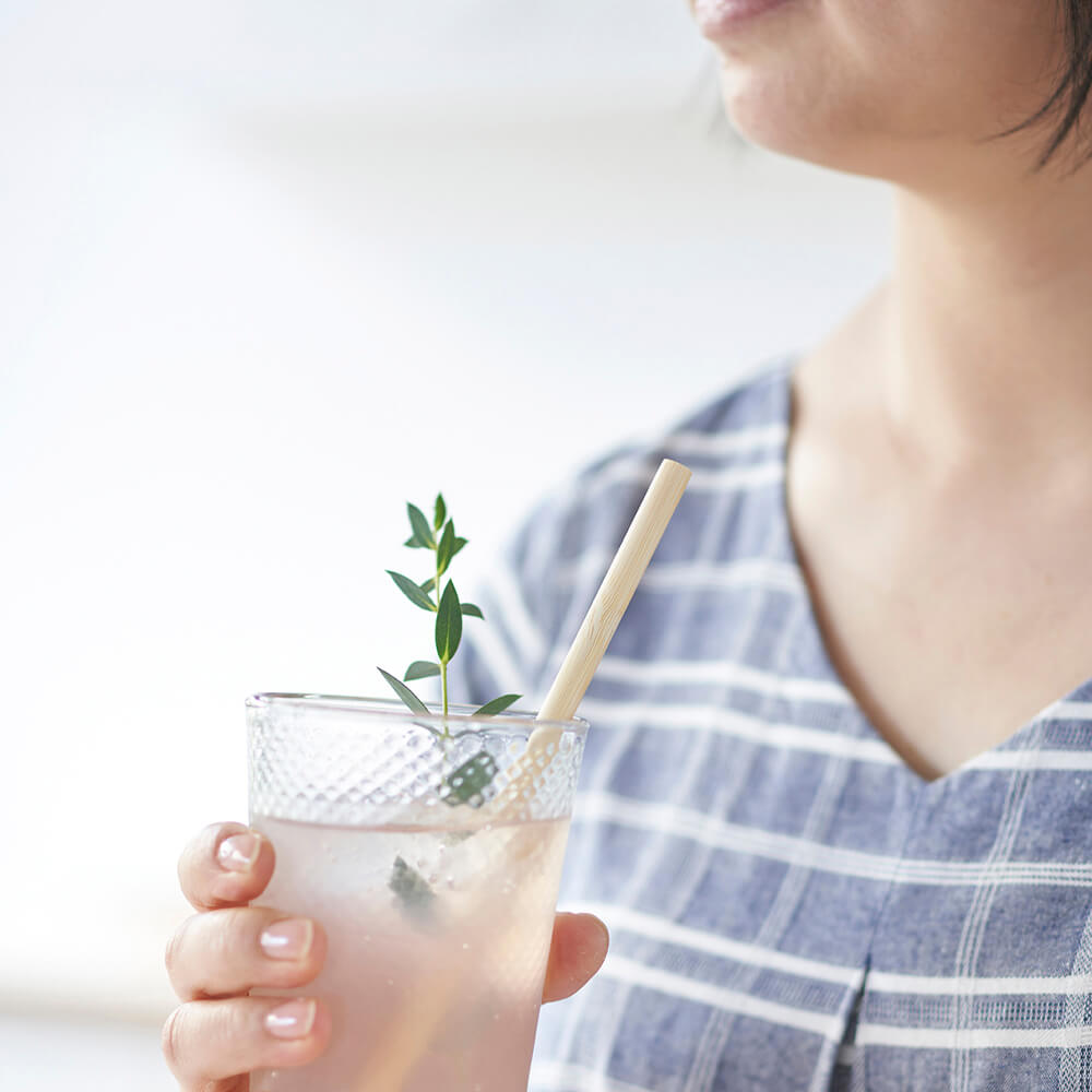 A person holds a glass filled with a pink beverage. They use a Single Use Bamboo Straw to sip from the beverage.