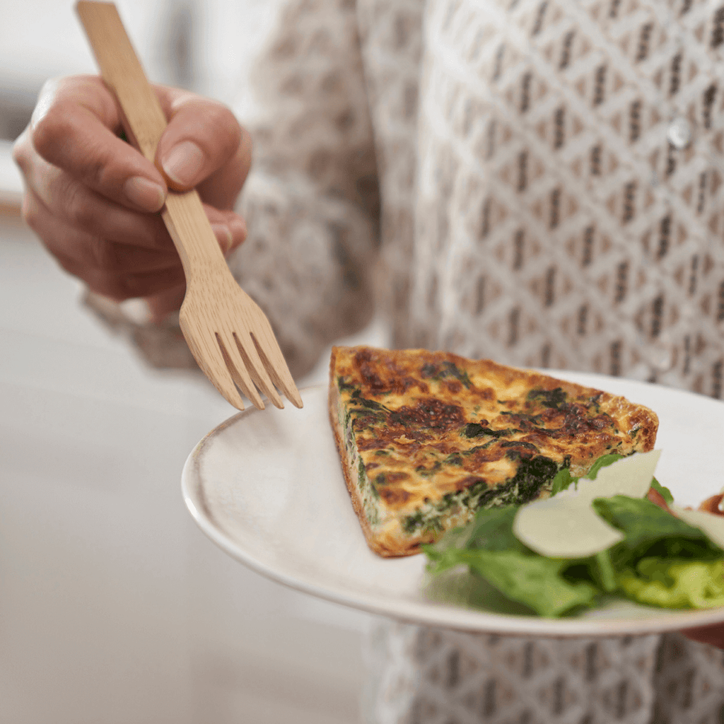 A person uses a bamboo reusable fork to eat a meal of quiche and salad. bambu
