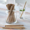 A large jar holds a handful of Precision Reusable Bamboo Straws. A glass with water sits next to the jar.