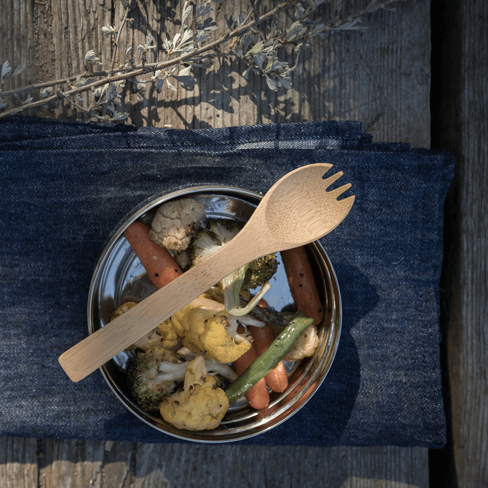 A bamboo large spork is ready to be picked up, sitting atop a container of roasted veggies.