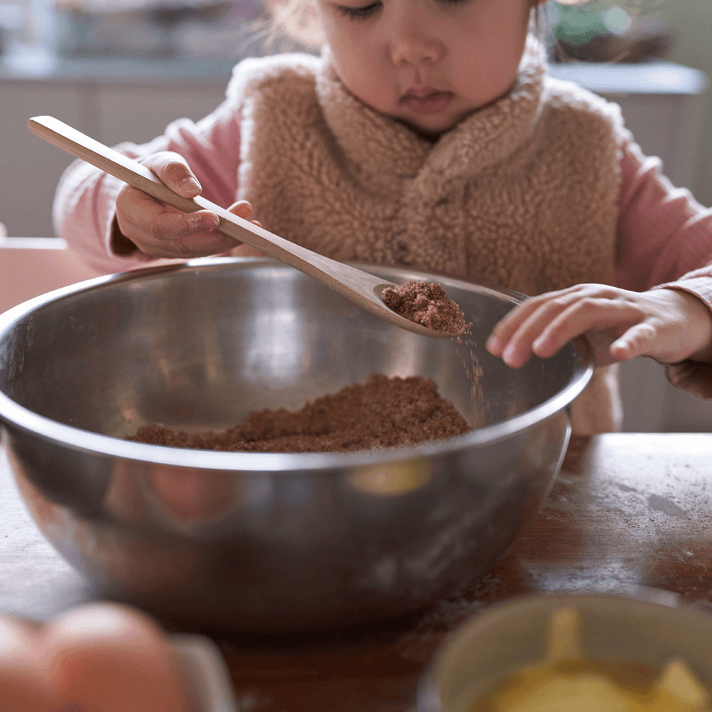A child uses the spoon from a Kids in the Kitchen set to stir ingredients in a bowl. bambu