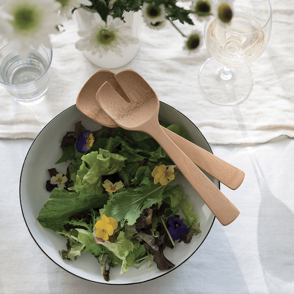 Bamboo Salad Servers are displayed on a salad bowl filled with leafy greens and edible flowers.