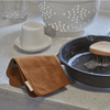 A nutmeg dishcloth is folded in half laid over the handle of a cast iron skillet.