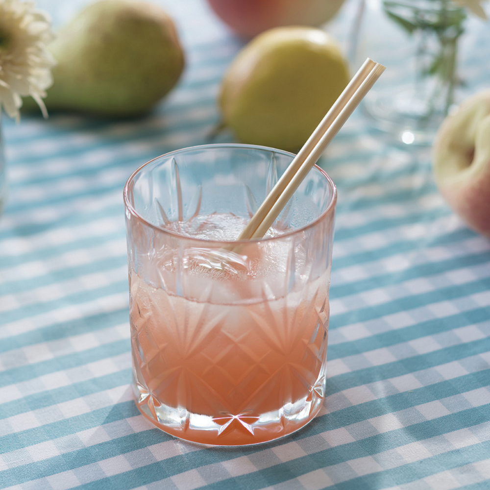 A cocktail glass with a pink beverage holds two 5-inch Biodegradable wheat straws.