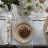 A 7" Veneerware® Round Bamboo Plate sits on a table with a cinnamon roll on top.
