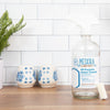 Meliora Cleaning Products: All-Purpose Home Cleaner in glass spray bottle sits on a counter near blue and white decorations.