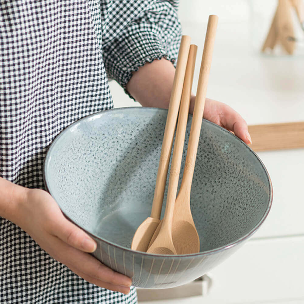 A bamboo tasting spoon, a spoontula, and a mixing spoon are displayed in a blue ceramic mixing bowl.