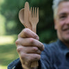 A man in a blue shirt holds a set of Bamboo Cutlery in their hand.