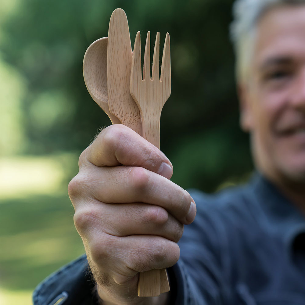 A man in a blue shirt holds a set of Bamboo Cutlery out.