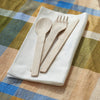 Veneerware® Bamboo Knife, Fork, Spoon set is placed on a bamboo napkin atop a bright colored table cloth.