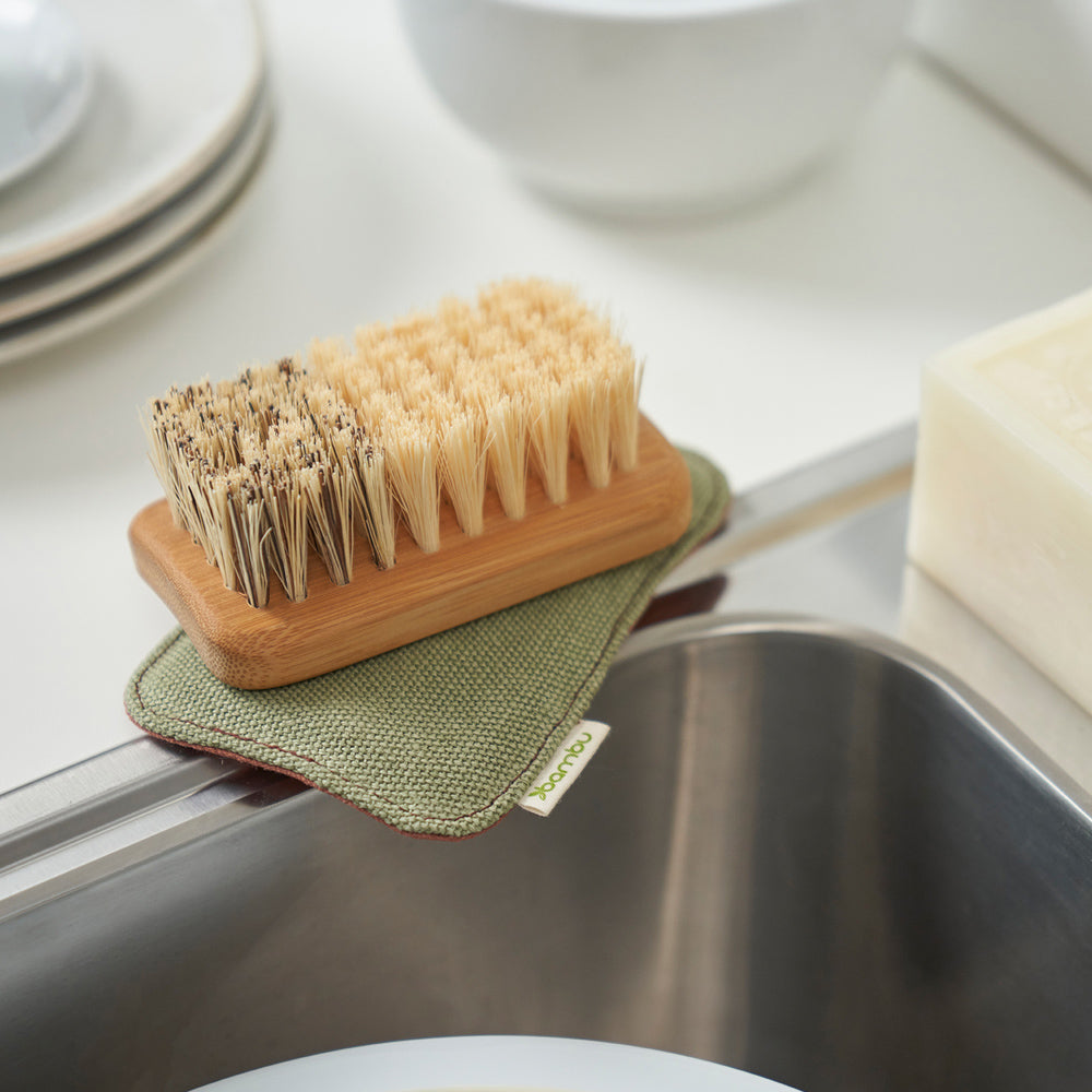 An All Purpose Cleaning Brush rests on top of a sponge at the edge of a sink.
