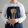 A person in a denim apron holds a Spoontula and two mixing spoons in front of themselves.