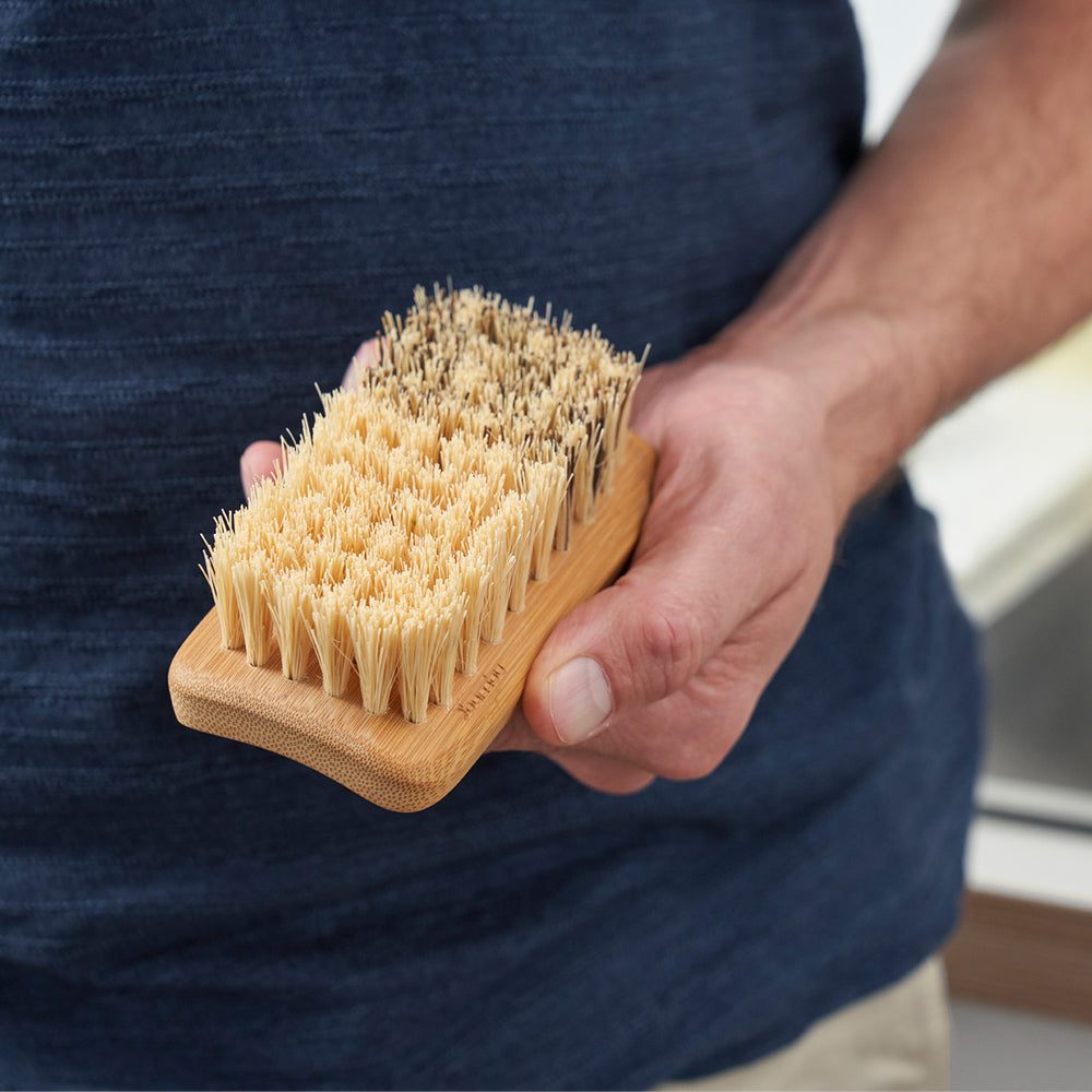 A person wearing a blue shirt holds an All Purpose Cleaning Brush at their hip.