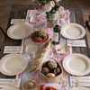 A wooden table is set with 11" Round Veneerware plates. Each setting is completed with a bamboo napkin, a set of bamboo cutlery, and a 5" square bread plate.