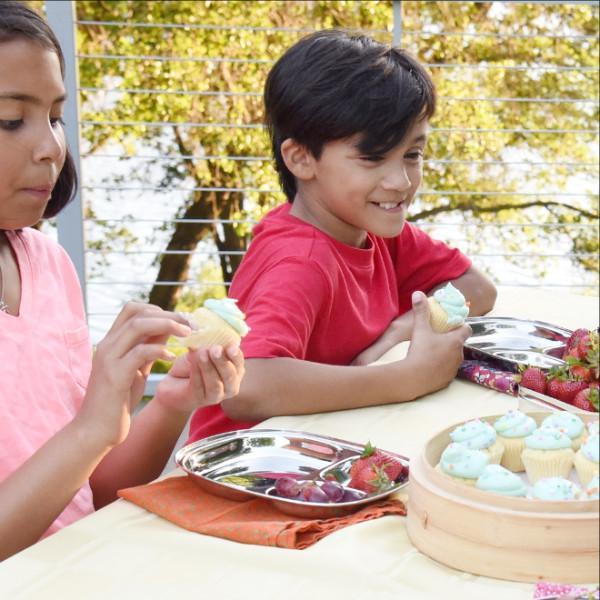 Two children eat miniature cupcakes from their Kids Lunch Trays. They also have a selection of berries and grapes on their trays.