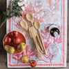 A Scraping Spatula, Mixing Spoon, and Spoontula are resting on a pink table runner next to a bowl of fruit.in utensil bouquet