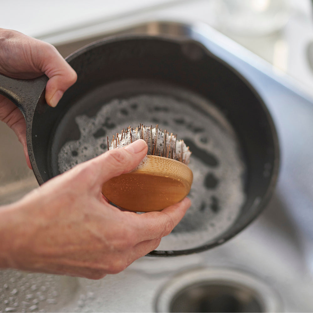 A person uses a Pot & Pan Scrub Brush to clean a cast iron pan in the sink.