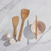 A Bamboo Wok Spatula, Rice Paddle, and pair of Chopsticks are displayed neat a pink and white ceramic bowl.